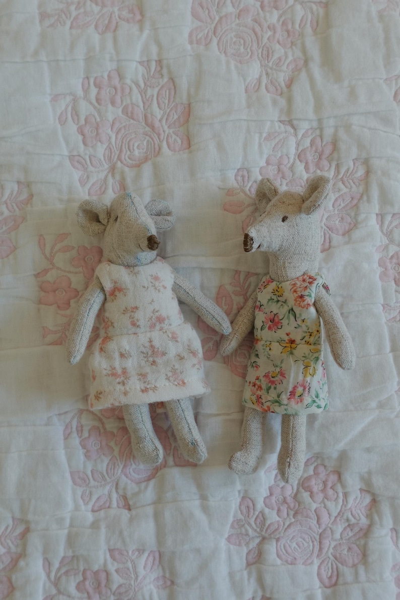 Puede incluir: Dos mu&ntilde;ecas de rat&oacute;n hechas a mano. Cada mu&ntilde;eca es gris con orejas grandes y un hocico largo. Una ratona viste un vestido blanco con estampado floral rosa, la otra viste un vestido floral con flores rosas, amarillas y verdes.