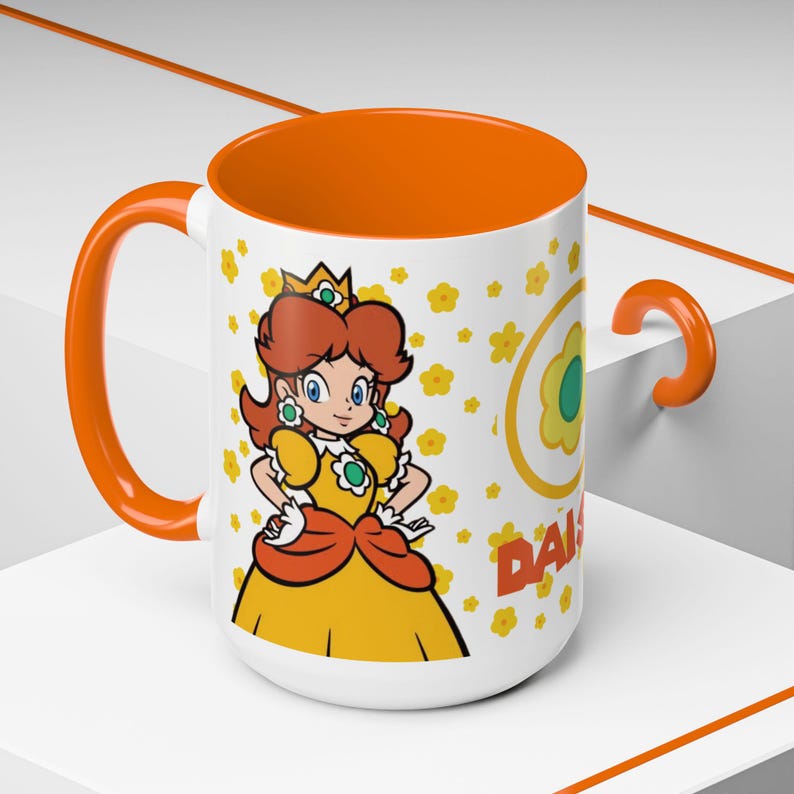 Pu&ograve; includere: Una tazza in ceramica bianca con un bordo e un manico arancioni. La tazza presenta un'immagine di cartone animato della principessa Daisy del franchise di Super Mario. Il design include un motivo a fiori gialli e il testo "Daisy".