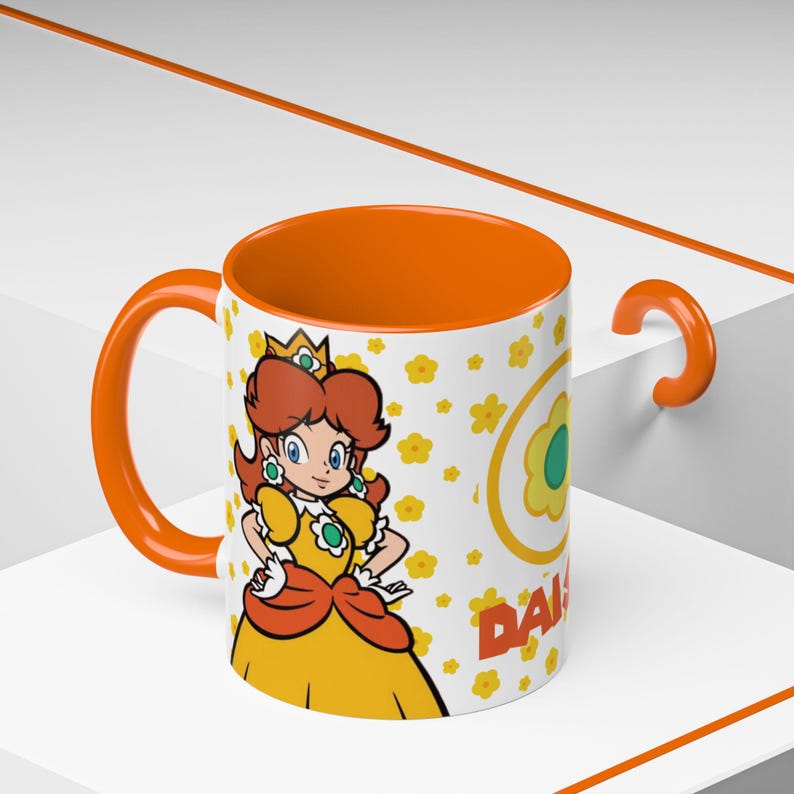 Pu&ograve; includere: Una tazza in ceramica bianca con un bordo e un manico arancioni. La tazza presenta un'immagine di cartone animato della principessa Daisy del franchise di Super Mario. La tazza ha uno sfondo bianco con fiori gialli e il testo "Daisy" in lettere arancioni.
