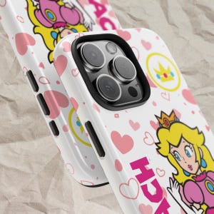 May include: White iPhone case with a pink and white pattern featuring Princess Peach from the Super Mario franchise. The case has a clear camera lens and the text "Peach" is printed on the bottom right corner.