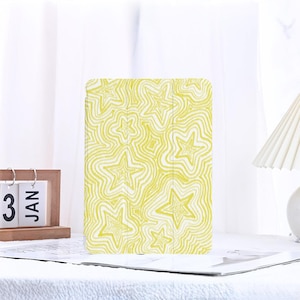 May include: Yellow and white patterned tablet case with a star design. The case has a folding cover. The star pattern is repeated across the entire surface of the case. The case is designed to protect a tablet.
