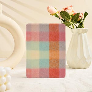 May include: A rectangular e-reader case featuring a soft-focus plaid pattern in pastel shades of pink, orange, yellow, blue, and gray. The surface has a textured, fabric-like appearance with a grid of intersecting colored squares.