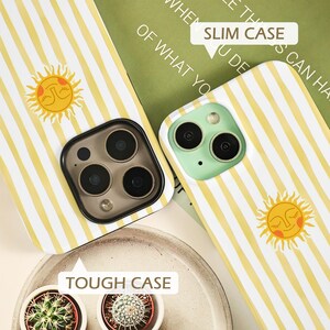 May include: Two phone cases with a yellow and white striped pattern and a smiling sun graphic. One case is labeled "SLIM CASE" and the other is labeled "TOUGH CASE". The phone cases have different camera designs.