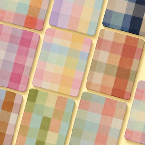 Könnte beinhalten: Eine Sammlung rechteckiger Untersetzer mit verschiedenen Karomustern in sanften Pastell- und gedeckten Erdtönen. Jeder Untersetzer zeigt ein Gitter aus sich überschneidenden farbigen Quadraten in Rosa, Gelb, Blau, Grün, Orange und Braun.