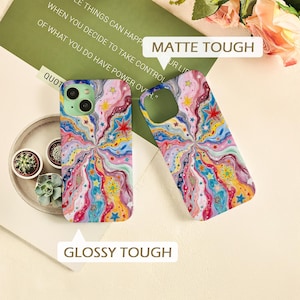 May include: Two phone cases featuring a vibrant, swirling pattern of multicolored wavy lines and scattered stars. One case is labeled MATTE TOUGH, while the other is labeled GLOSSY TOUGH. The design incorporates shades of pink, blue, yellow, and red.