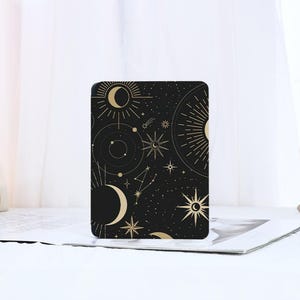 Puede incluir: Una cubierta de cuaderno de temática galáctica negra y dorada con un patrón celestial de lunas, estrellas y rayos de sol.