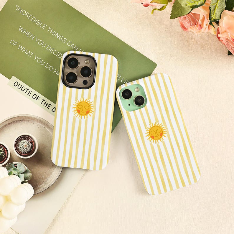 May include: Two phone cases with a yellow and white striped pattern and a smiling sun graphic. The cases have a protective design and are likely for a smartphone. The background includes a green card with text.