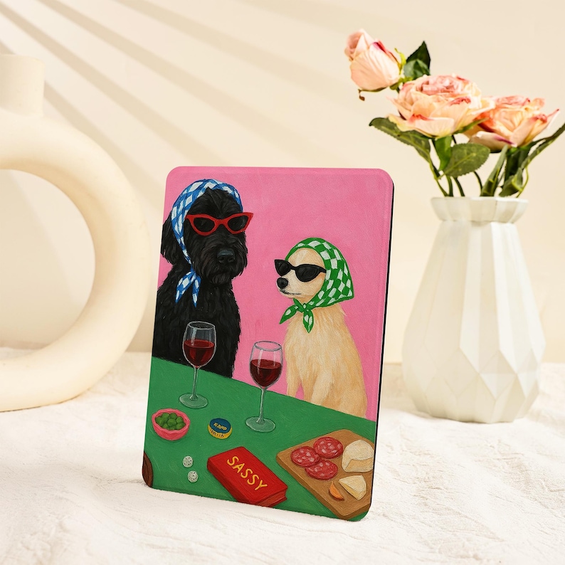 Pu&ograve; includere: Una stampa artistica rettangolare con due cani con occhiali da sole e foulard, che si godono vino e snack. L'opera d'arte ha uno sfondo rosa e un tavolo verde con la parola "SASSY" su una scatola rossa.