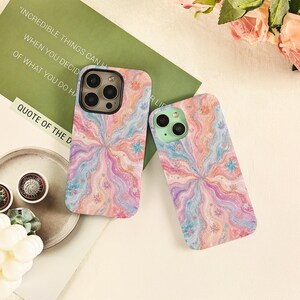May include: Two smartphone cases featuring a swirling, marbled pattern in pastel shades of pink, blue, and orange. The designs include small, scattered star-like accents. One case has a dark camera housing, while the other has a light green housing.