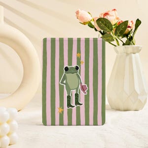 May include: A rectangular decorative item featuring a frog illustration on a green and pink striped background. The frog wears cowboy boots and a hat. Yellow star accents are included.