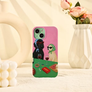 May include: Pink phone case featuring a whimsical illustration of two dogs wearing sunglasses and headscarves, enjoying wine. The word "SASSY" is printed on a red card. The case has a green camera module and a green border.