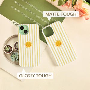 May include: Two phone cases with a yellow and white striped pattern and a smiling sun graphic. One case is upright, and the other is angled. The text "MATTE TOUGH" and "GLOSSY TOUGH" are visible.