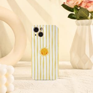 May include: A white and yellow striped phone case featuring a smiling sun graphic. The case has a vertical stripe pattern and a yellow sun with a smiling face in the center. The case is designed for a smartphone.