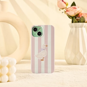 May include: A phone case with a vertical pink and white striped pattern. The case features a cartoon illustration of a white duck with a blue bow. The phone case has a green camera module.