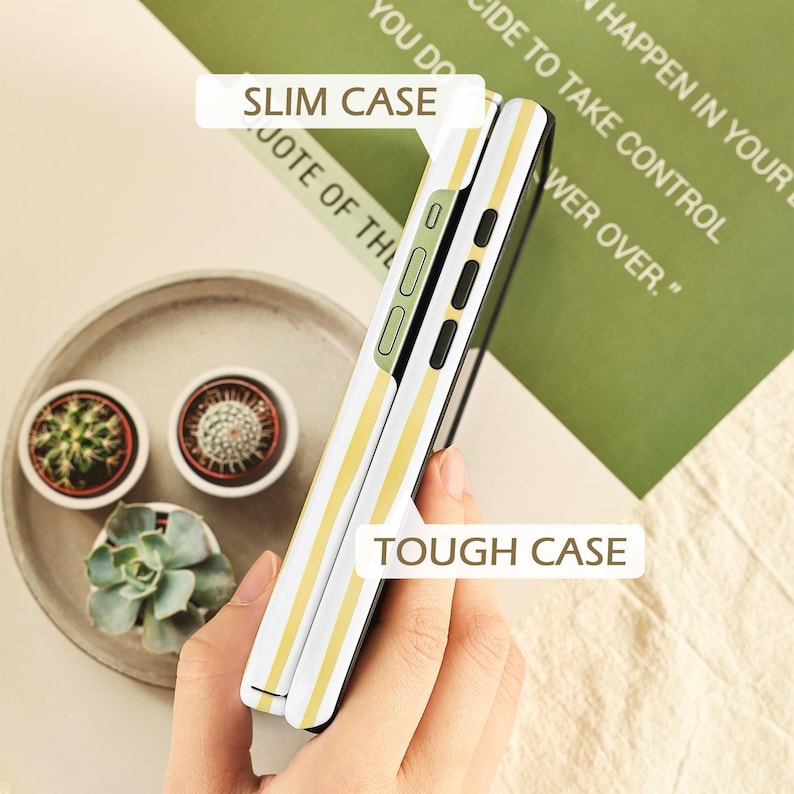 May include: A white and yellow striped phone case with the text "SLIM CASE" and "TOUGH CASE". The phone case is held in a person's hand. The background includes a green paper with text and a tray with small potted plants.