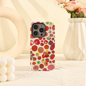May include: A white phone case adorned with a vibrant pattern of various tomatoes in shades of red, orange, and green. The design includes different tomato shapes and sizes, creating a playful and colorful aesthetic. The case has a glossy finish.