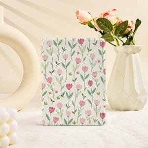 May include: A rectangular, floral-patterned item featuring a repeating design of pink and red tulips with green stems and leaves on a cream background. The item is upright, with a soft, matte finish. A white vase with pink flowers is in the background.