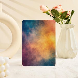 May include: A rectangular e-reader cover featuring a vibrant, abstract smoke-like pattern that blends deep shades of blue, purple, orange, and yellow across its surface. The design displays a smooth, gradient transition of colors.