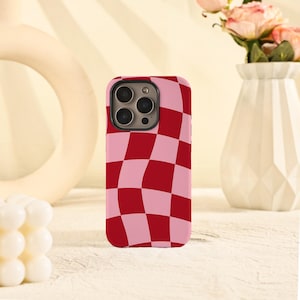 May include: A smartphone case featuring a red and pink chequered design. The case has a camera aperture and is designed to fit a mobile phone. The case is made of a smooth material with a glossy finish.