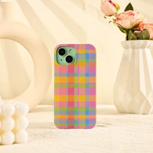 May include: A colorful phone case with a plaid pattern in shades of pink, orange, yellow, green, and blue. The phone case has a mint green camera lens area and is sitting on a white surface.