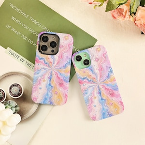May include: Two mobile phone cases featuring a swirling, marbled pattern in pastel shades of pink, blue, and yellow. The design is accented with small, scattered star-shaped glitter elements throughout the surface, creating a vibrant, multi-colored aesthetic.
