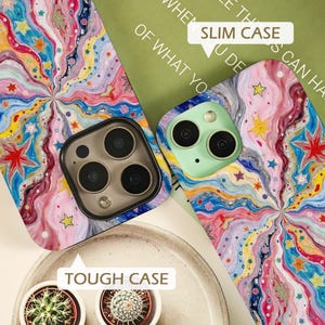 May include: Two phone cases featuring a vibrant, swirling pattern of pink, blue, yellow, and white waves decorated with small colorful stars. One case is labeled as a Slim Case, while the other is identified as a Tough Case, each with camera cutouts.