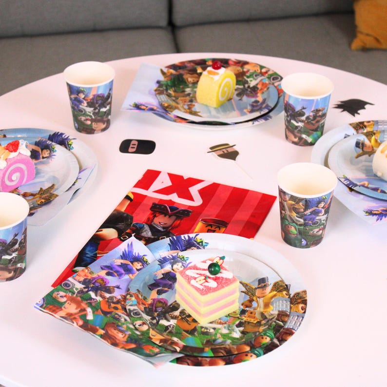 May include: A party table setting with plates, cups, and napkins featuring a colorful cartoon design. The plates hold small cakes and pastries. The table is set for a celebration.