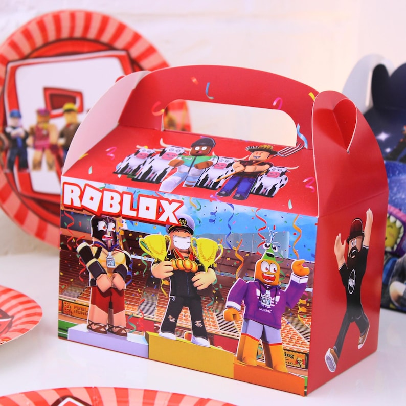 May include: Red Roblox-themed party favor box with a handle, featuring colorful cartoon characters and the Roblox logo. The box has a stadium background and is decorated with confetti.