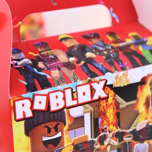 May include: Red Roblox-themed gift box featuring Roblox characters and the Roblox logo in white. The box has a handle and is decorated with images of characters and a burning building. The overall design is vibrant and eye-catching.
