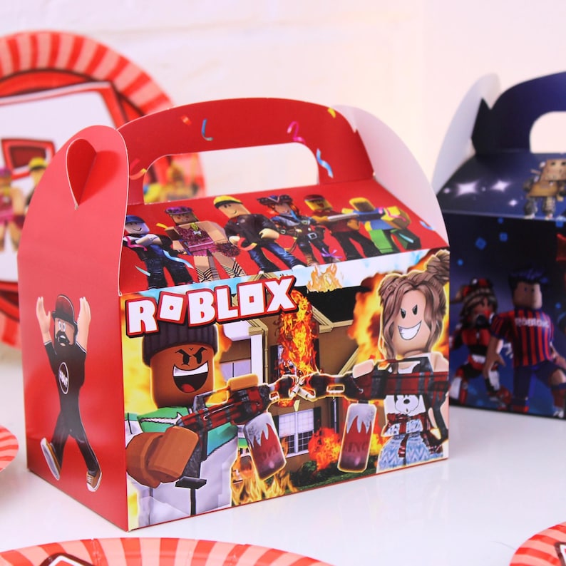 May include: Red party favor box with a handle, featuring Roblox characters and the Roblox logo. The box has a colorful design with action scenes and characters from the popular online game.