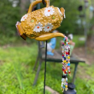 Vindklocka och solfångare i tekanna med kola och vit blomma.