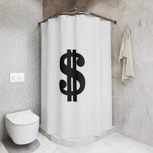 Puede incluir: Cortina de ducha blanca con un gran signo de dólar negro impreso en ella. La cortina de ducha está colgada en un baño con un inodoro blanco y paredes de azulejos blancos.