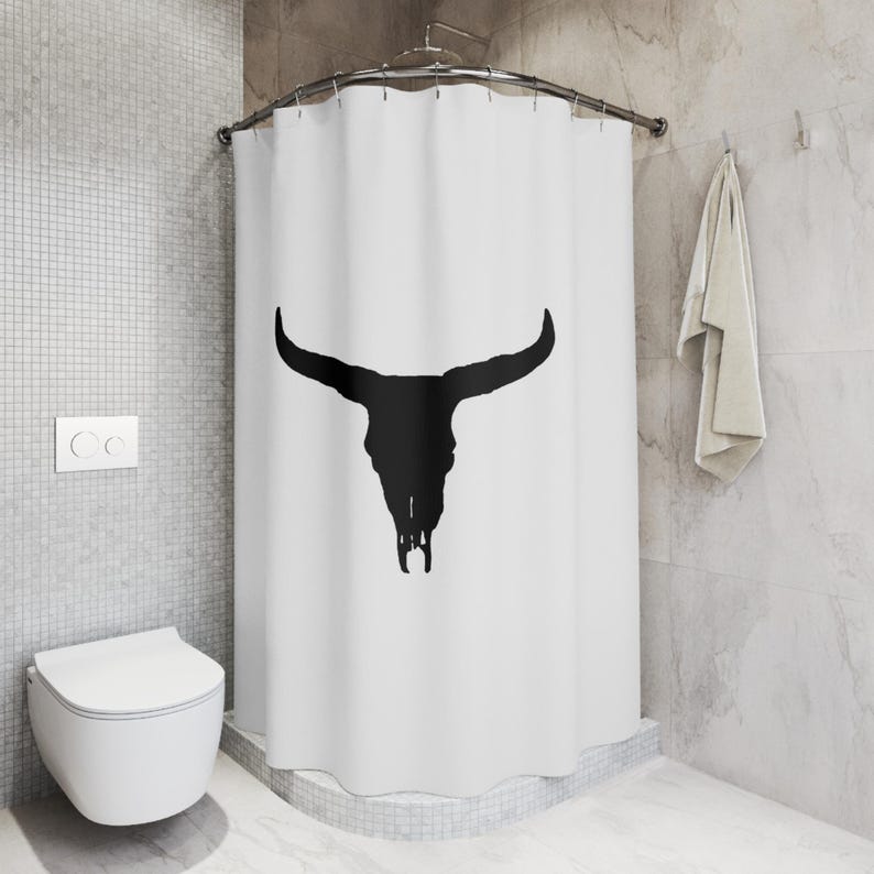 May include: White shower curtain with a black silhouette of a bull skull. The shower curtain is hung on a curved shower rod.