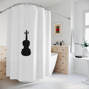 May include: White shower curtain featuring a black violin silhouette. The curtain hangs from a curved, silver-colored rod. The bathroom has a white tub, a small table, and a framed artwork.