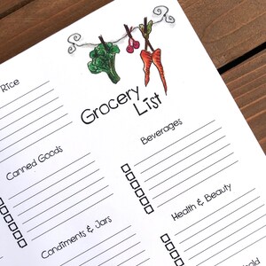 May include: A white grocery list with the title "Grocery List" in black script. The top of the list features a whimsical illustration of vegetables hanging on a washing line. The list includes sections for various grocery items with checkboxes.