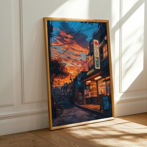 Puede incluir: Una pintura enmarcada que representa una escena callejera en Jap&oacute;n. La calle est&aacute; bordeada de edificios, algunos de los cuales tienen letreros en japon&eacute;s. El cielo es de un naranja y rosa vibrantes, y hay nubes en el cielo. La pintura est&aacute; en un marco de madera.