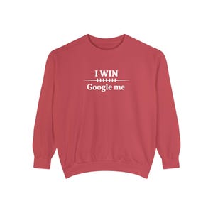 May include: A red sweatshirt with long sleeves. The white text "I WIN" is above a horizontal line, and below the line is the text "Google me". The sweatshirt is a solid color.