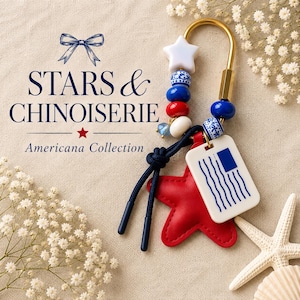 May include: A keychain featuring a gold-toned metal hook, a white star bead, blue and white patterned beads, solid red and blue beads, a red leather star charm, and a white rectangular tag with a blue graphic of a flag. Text reads STARS & CHINOISERIE.