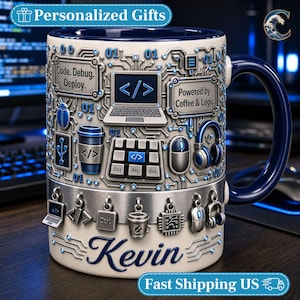 May include: A ceramic mug with a dark blue interior and handle, featuring a light-colored exterior with a 3D-style circuit board pattern. It displays icons of a laptop, coffee cup, mouse, and headphones, with text reading Code. Debug. Deploy. and Powered by Coffee & Logic. The name Kevin is printed in blue script at the base, accented by hanging metallic charms.