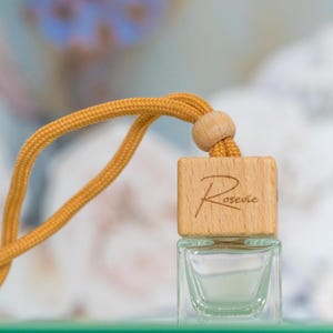 May include: A small, clear glass bottle with a wooden cap and a yellow string. The wooden cap has the word "Rosevie" engraved on it.
