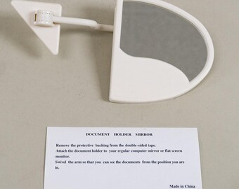 May include: White plastic document holder mirror with a swivel arm. The mirror is attached to the arm with a hinge. The arm is attached to a base that has adhesive tape on the back. The base is labeled "DOCUMENT HOLDER MIRROR". The instructions say to remove the protective backing from the double-sided tape, attach the document holder to your regular computer monitor or flat screen monitor, and swivel the arm so that you can see the documents from the position you are in. The label also says "Made in China" and "STAT0012".