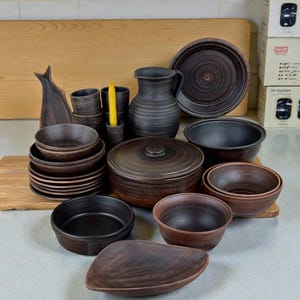 以下が含まれることがあります： 手作りの濃い茶色の陶器食器のコレクション。セットには、お皿、ボウル、ピッチャー、蓋付きのキャセロール皿、サービングピースが含まれます。素朴でアースカラーの陶器は、自然な家の装飾スタイルに最適です。