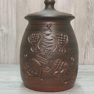 Puede incluir: Un tarro de cerámica marrón con tapa. El tarro presenta diseños de abejas en relieve alrededor del cuerpo. El tarro mide aproximadamente 20 cm de alto y 15 cm de ancho, con un esmalte marrón oscuro.
