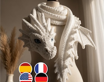May include: A white crocheted scarf shaped like a dragon, featuring a detailed head with blue eyes, textured scales, and pointed wings along the length of the scarf. The piece is crafted with a thick yarn texture and wraps around a mannequin neck.