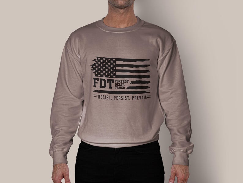 May include: A tan long-sleeve sweatshirt with a black and white American flag graphic. The text "FDT Fox Trot Delta Tango Resist, Persist, Prevail" is printed below the flag.