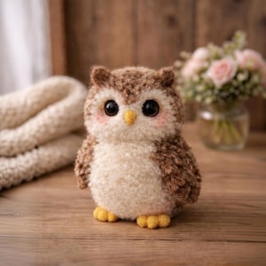 May include: A handcrafted owl figurine with a plush, textured appearance. The owl features a combination of brown and cream-colored yarn, large black eyes, a yellow beak, and pink cheeks. The owl's feet are yellow. The figurine is a decorative item.
