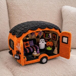 May include: A crocheted Halloween-themed camper van in orange and black with an open door. The interior features a small ghost, a pumpkin, a broom, a cauldron with green contents, a striped sofa with pillows, and a sign that reads BOO.