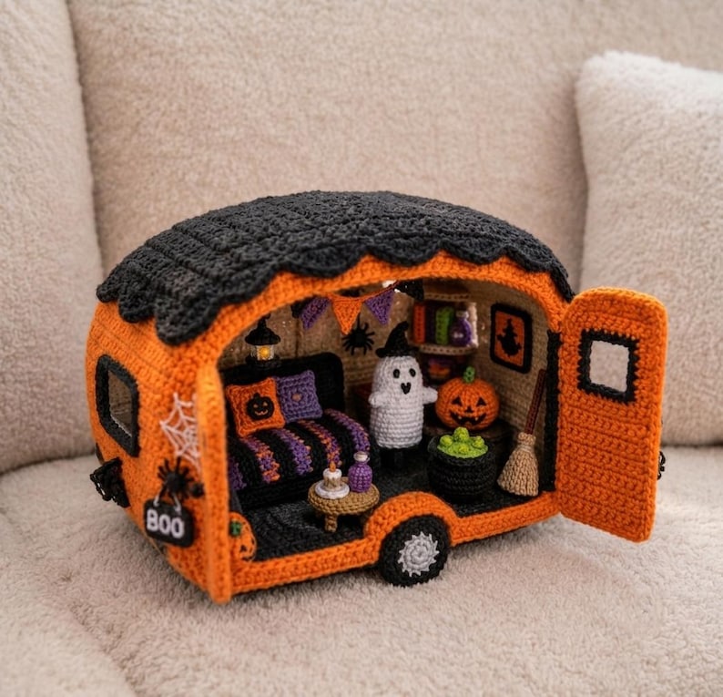 May include: A crocheted Halloween-themed camper van in orange and black with an open door. The interior features a small ghost, a pumpkin, a broom, a cauldron with green contents, a striped sofa with pillows, and a sign that reads BOO.