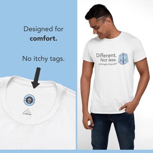 Pu&ograve; includere: Una t-shirt bianca con il testo Different. Not less. e un'illustrazione di una camicia azzurra con il nome Temple Grandin. L'interno del colletto mostra un logo circolare stampato con l'icona di una lampadina e nessuna etichetta.