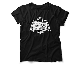 Può includere: T-shirt nera con grafica bianca raffigurante un'aquila con le ali spiegate, uno stendardo con la scritta "Nosotros el pueblo" e tre stelle. Il disegno è centrato sul davanti della maglietta.